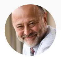 Close-up of a smiling middle-aged man with a beard, wearing a white shirt and patterned tie.