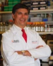 A woman in a white coat with a red tie, standing in a pharmacy or laboratory setting.