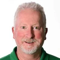 Close-up portrait of a smiling man with gray hair and a gray beard, wearing a green collared shirt.