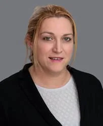 A woman with blonde hair wearing a black blazer and white top, smiling at the camera.