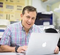 A man in a plaid shirt sitting at a desk using a laptop in an office setting.