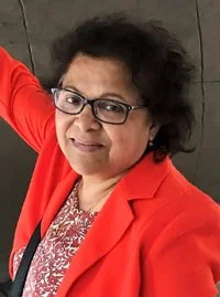 A woman wearing glasses and a red blazer, smiling and looking at the camera.