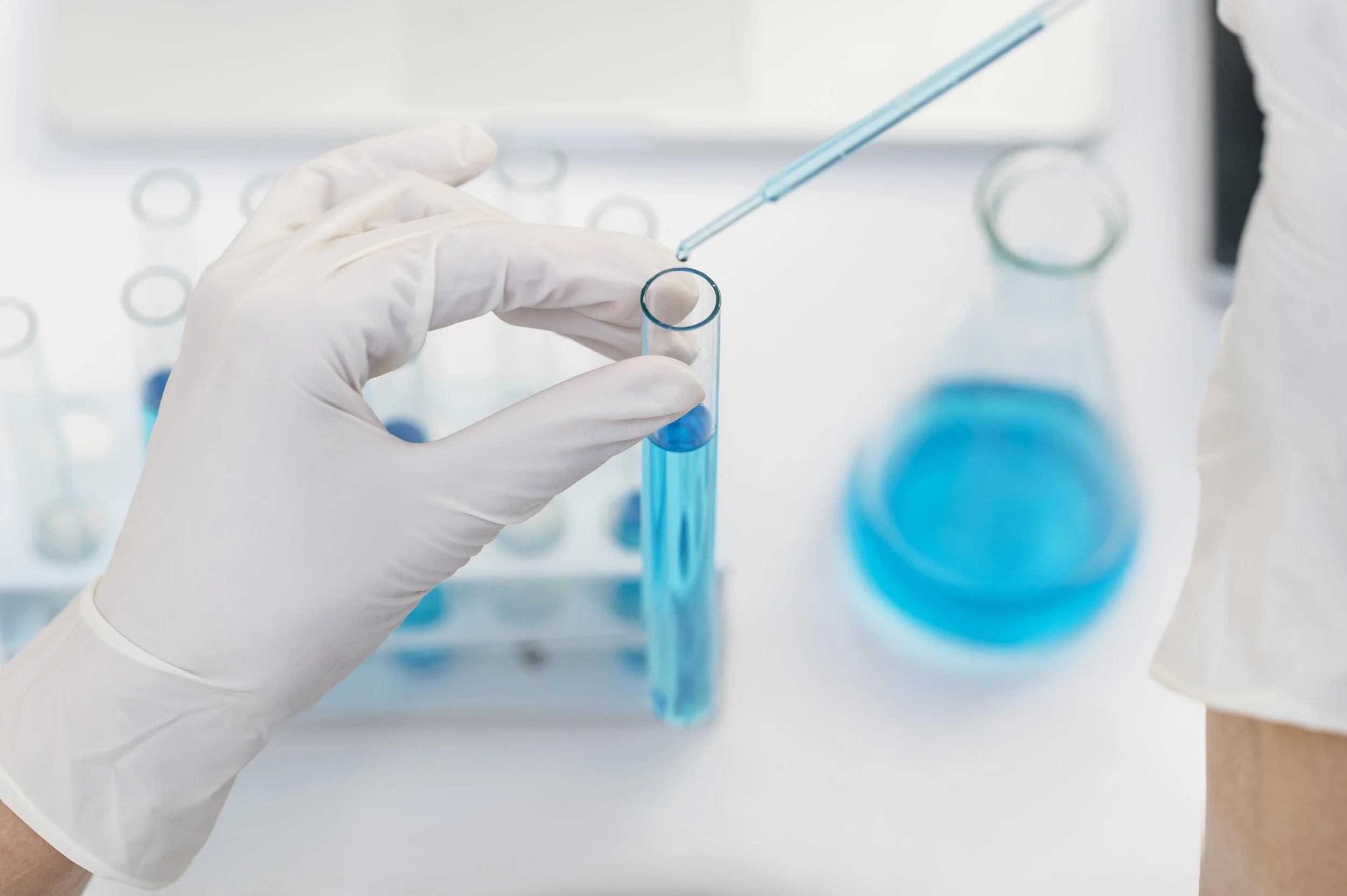 A scientist wearing white gloves handling a test tube filled with blue liquid in a laboratory setting.