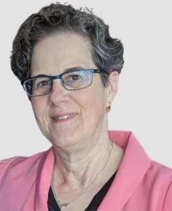 Close-up of an older woman with short, curly gray hair wearing glasses and a pink cardigan.