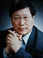 A man with black hair wearing a dark suit and tie, posing with hands clasped together, looking at the camera.