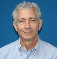 Headshot of a middle-aged man with gray hair, wearing a light blue collared shirt, against a blue background.