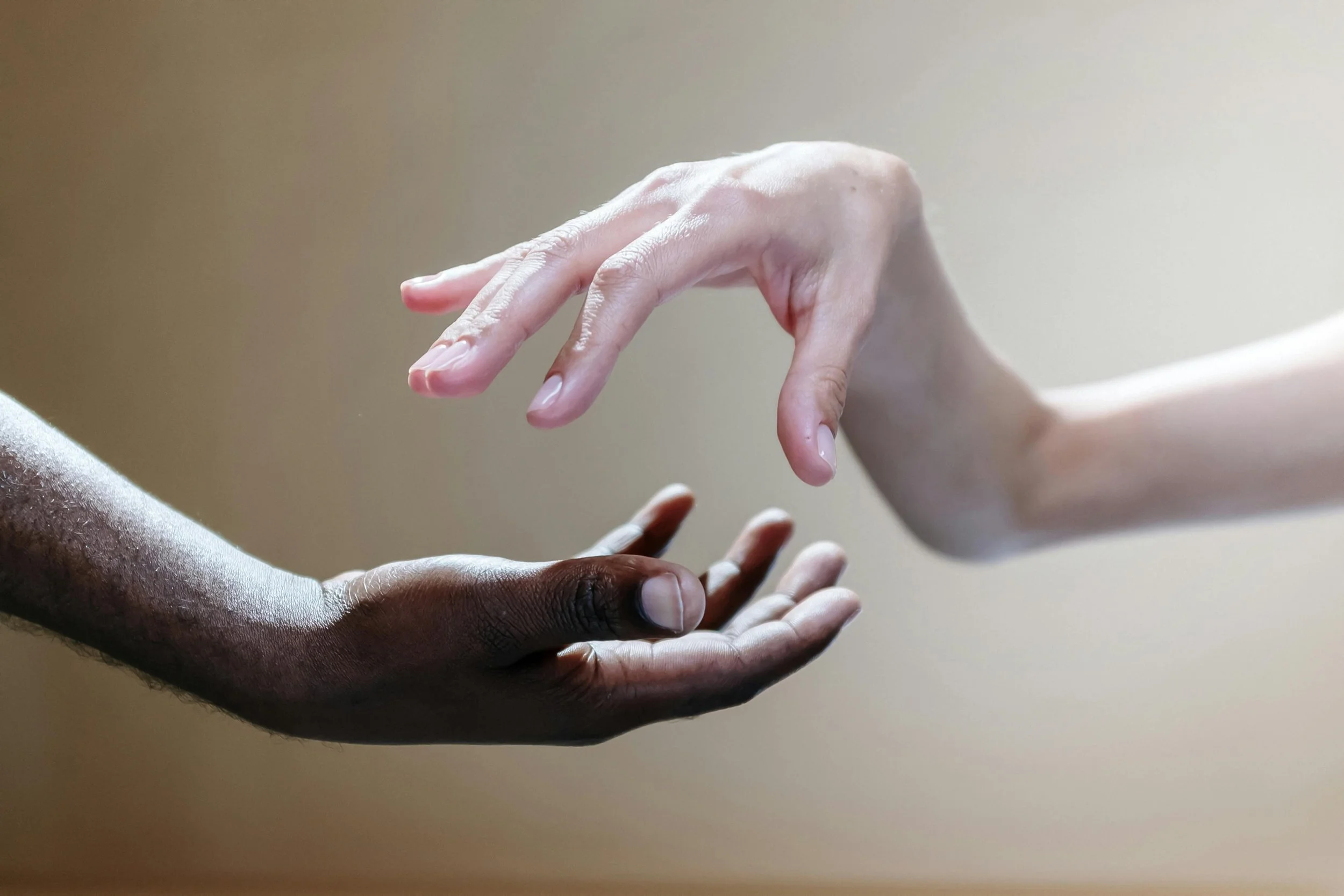 Two hands reaching towards each other, one dark-skinned and one light-skinned, with minimal background.