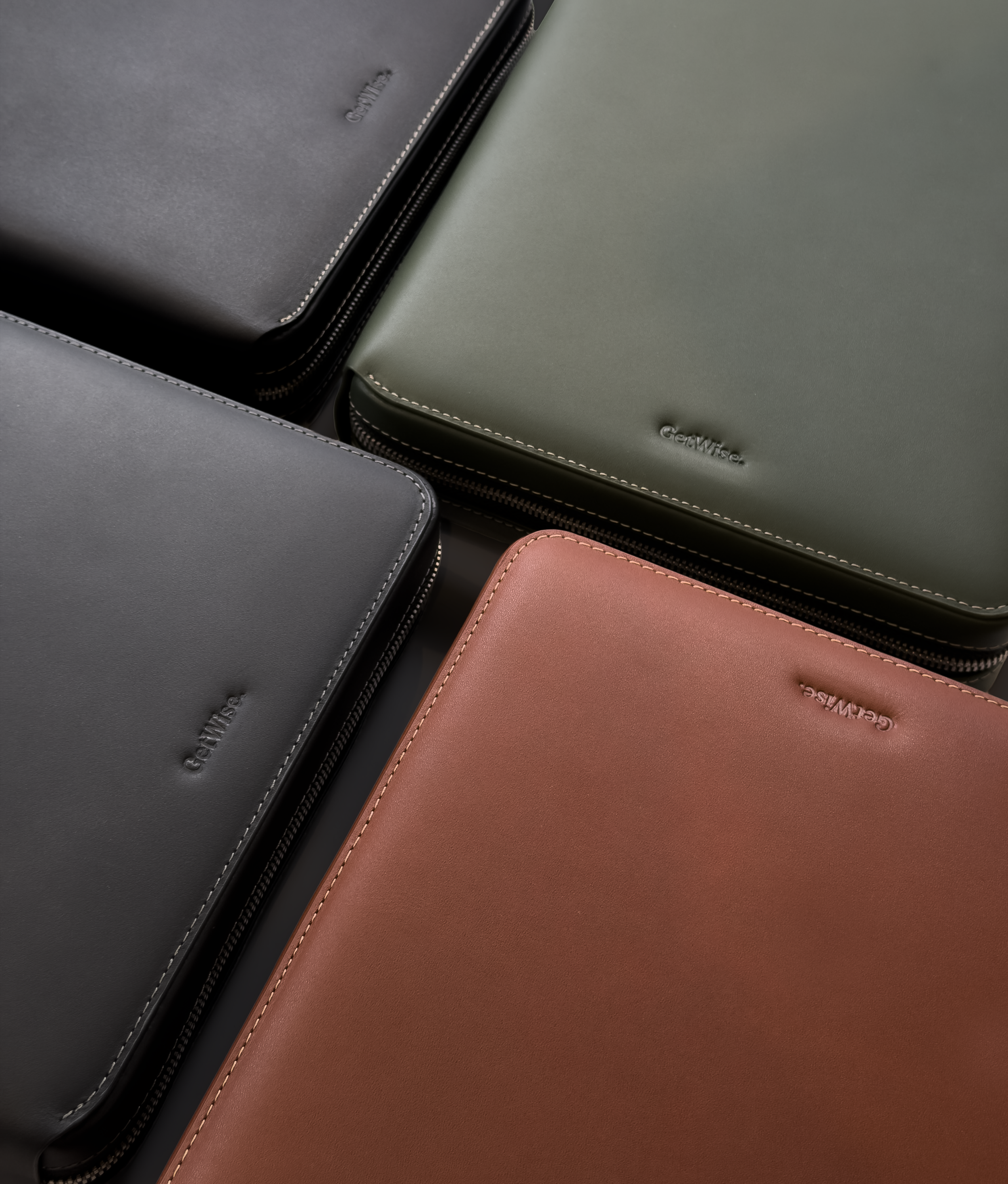 Close-up of four leather wallets in gray, black, green, and pink, with visible stitching and zipper details.
