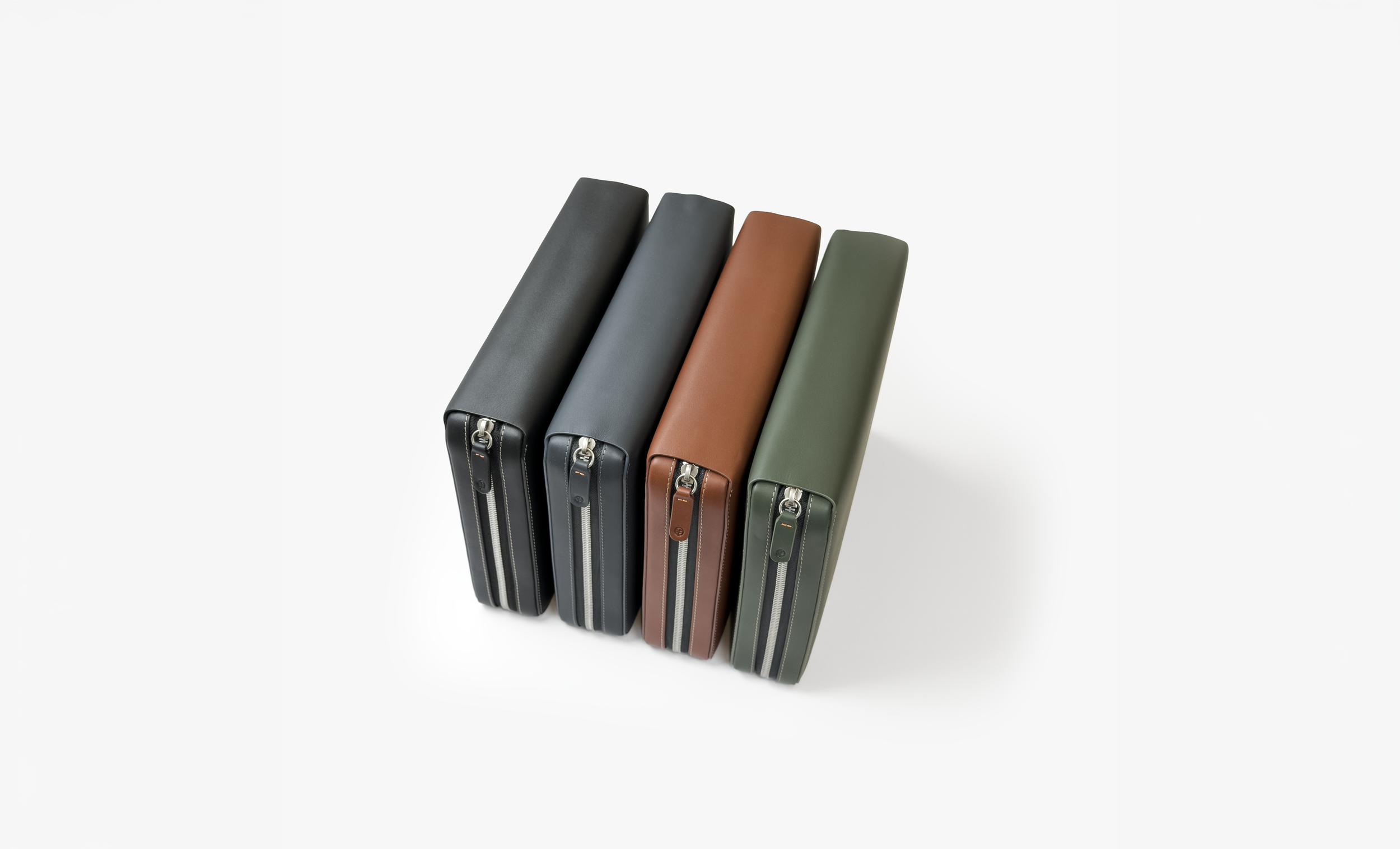 Four pencil cases in black, dark gray, brown, and green, arranged diagonally on a white background.