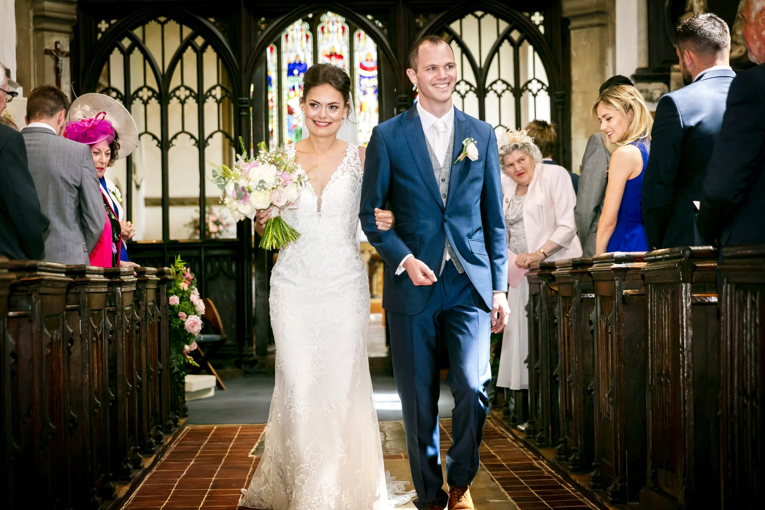 A newlywed couple walking down the aisle inside a church after their wedding ceremony, surrounded by friends and family.