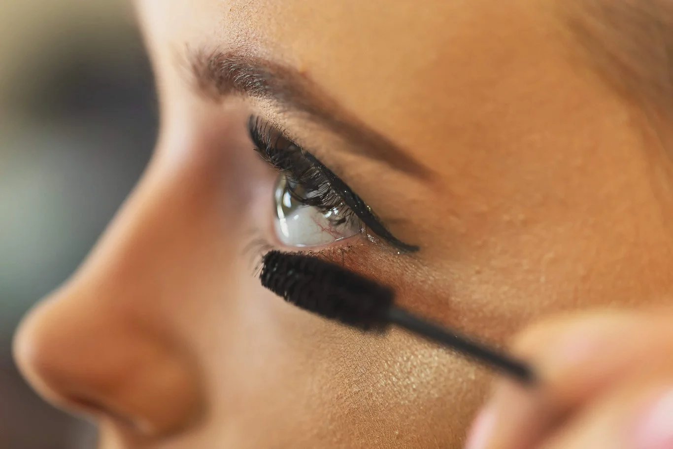 Close-up of a person's face with eyeliner and mascara application, showing the eye, eyebrow, and part of the nose.