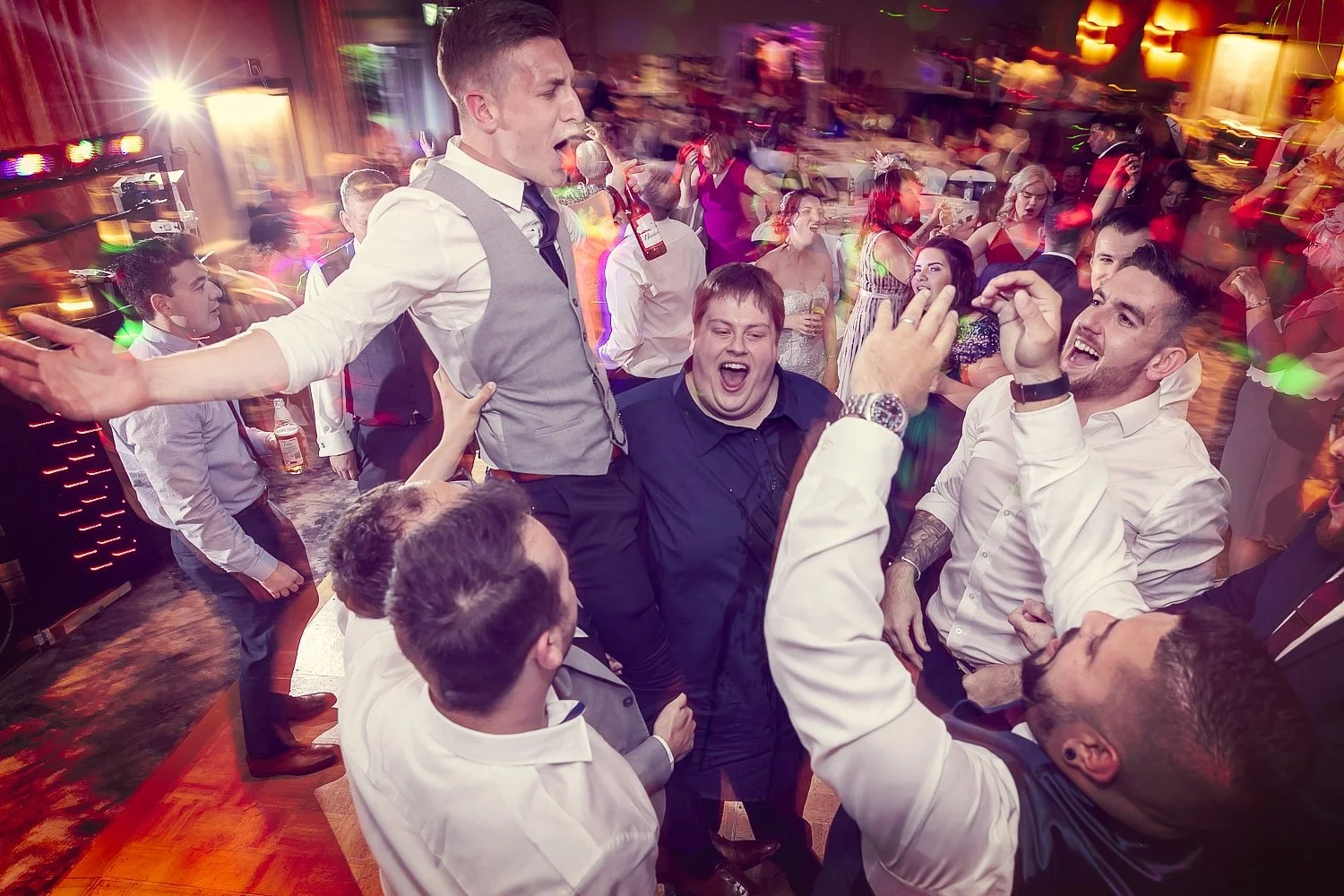 Group of people dancing and celebrating at a party with colorful lights.