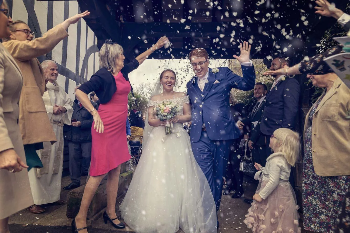 A wedding celebration with a bride and groom walking happily under a confetti shower, surrounded by family and friends.