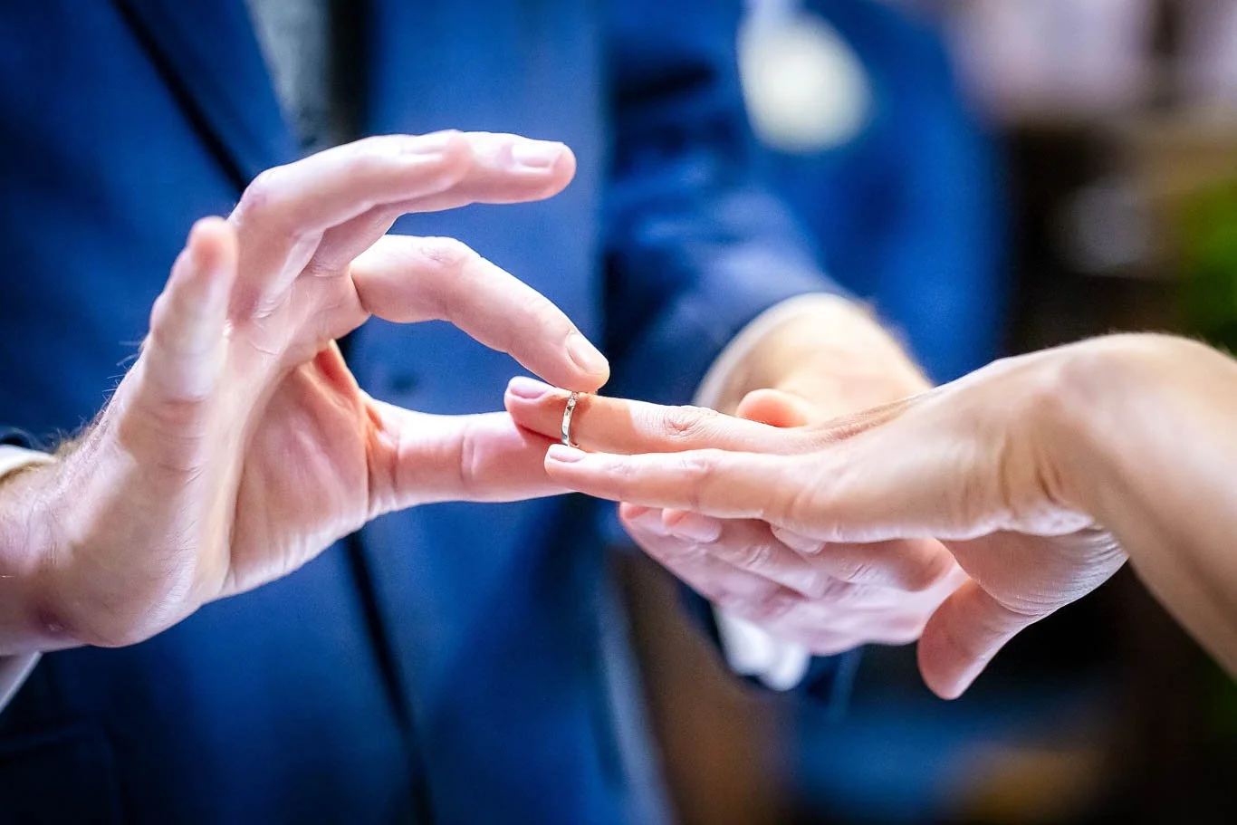 Close-up of two people exchanging wedding rings, with one person placing a ring on the other's finger.