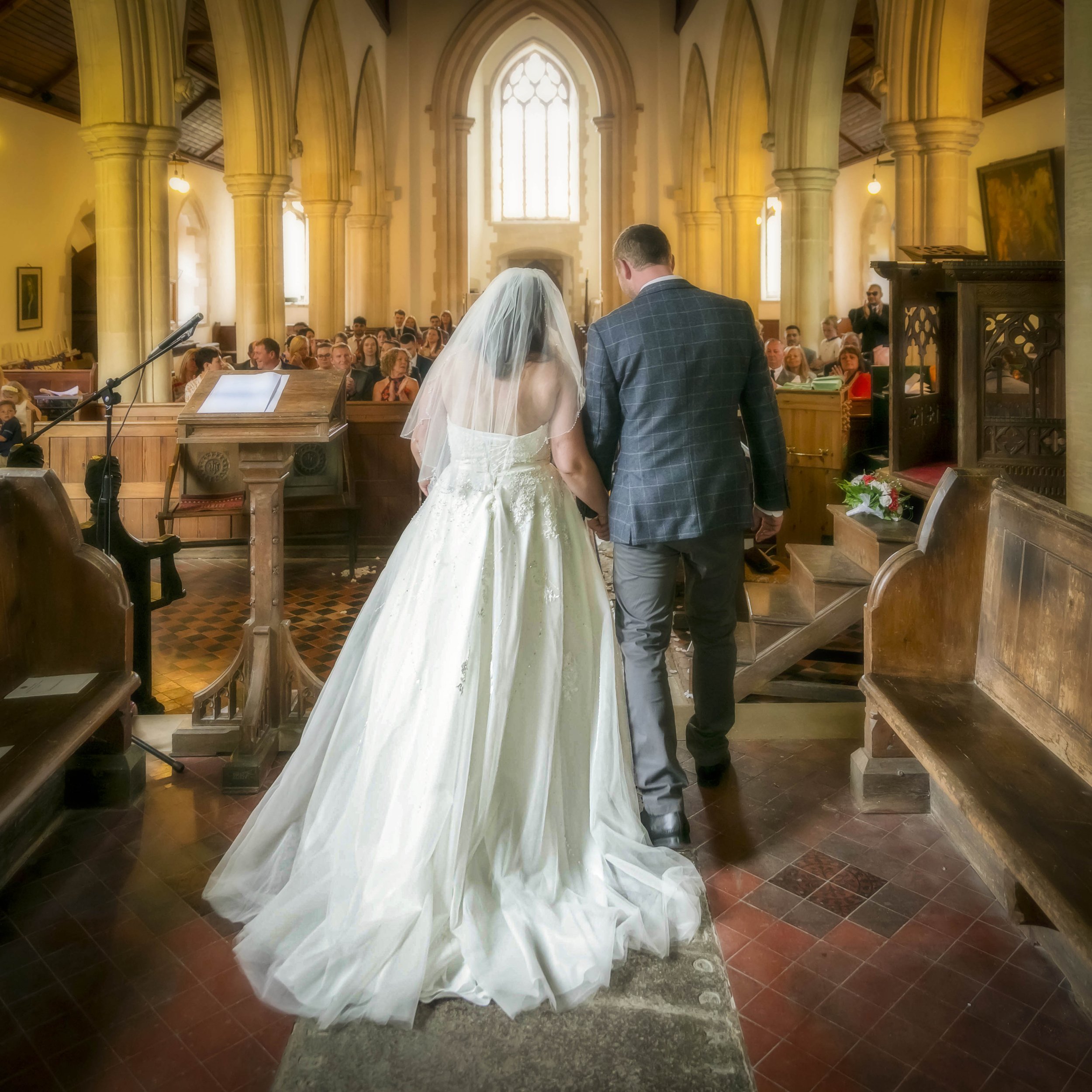 A bride and groom holding hands during their wedding ceremony in a church, with guests seated in the background.