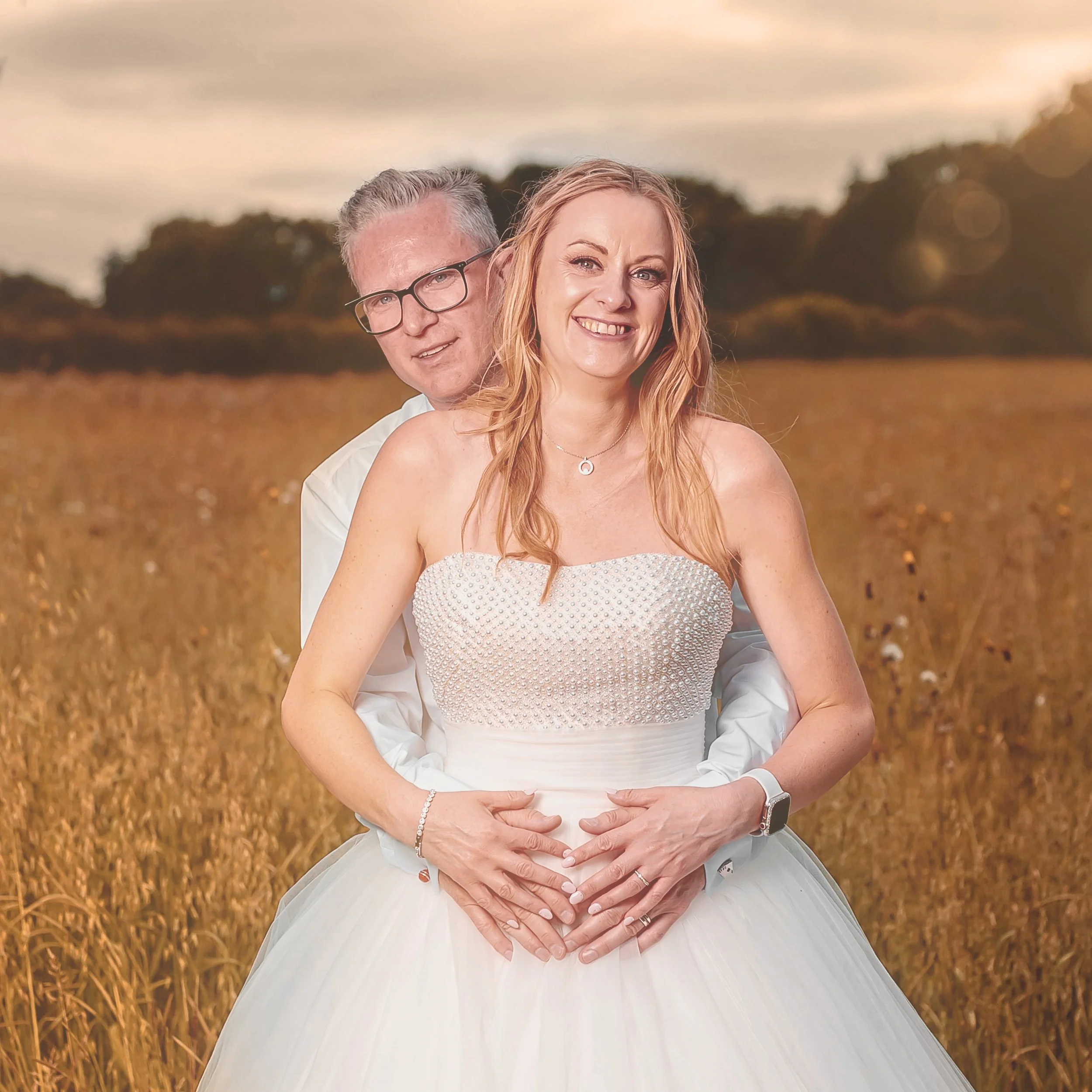 A couple on their wedding day standing in a field during sunset.