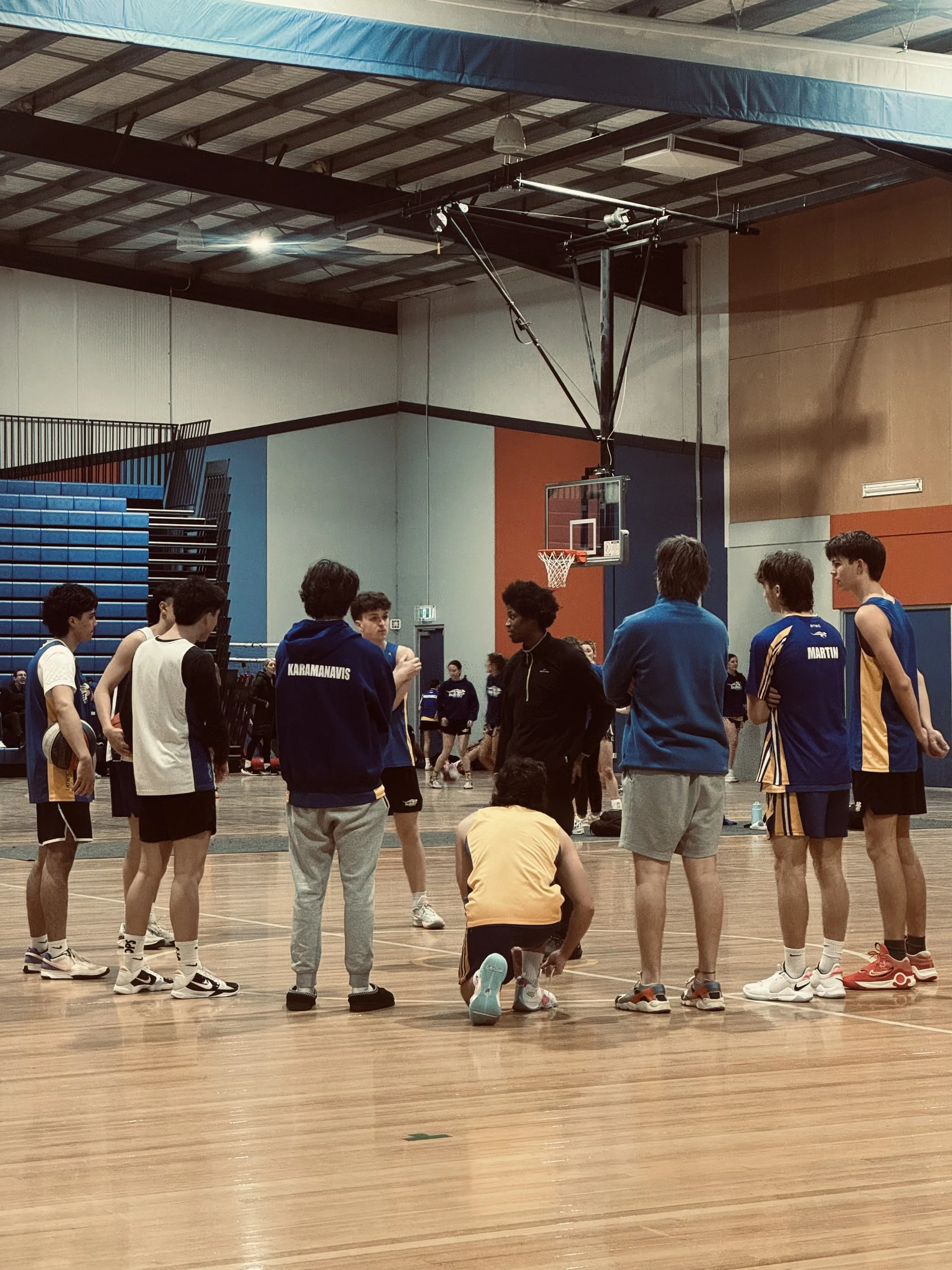 A group of young basketball players and coaches gathered in a gym, listening to a coach during a team huddle.