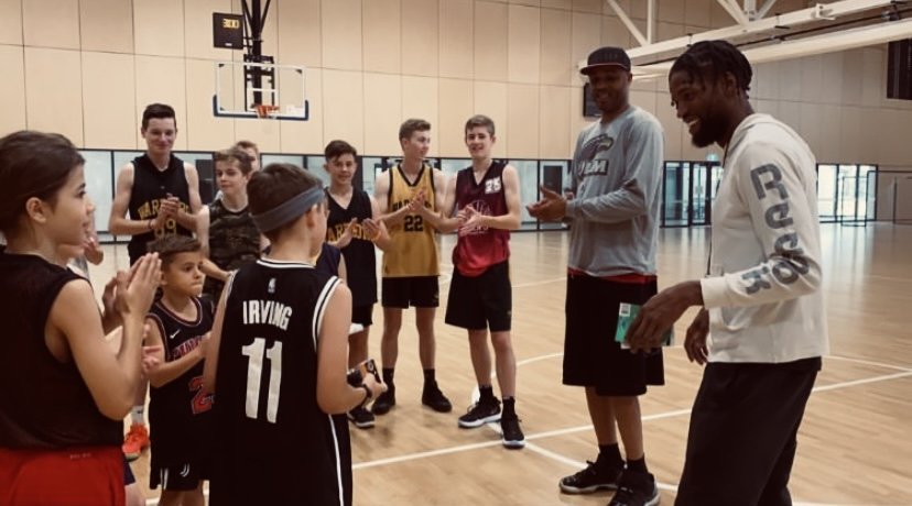Basketball team of children gathered on an indoor court, listening to two adult coaches before or after a game or practice.