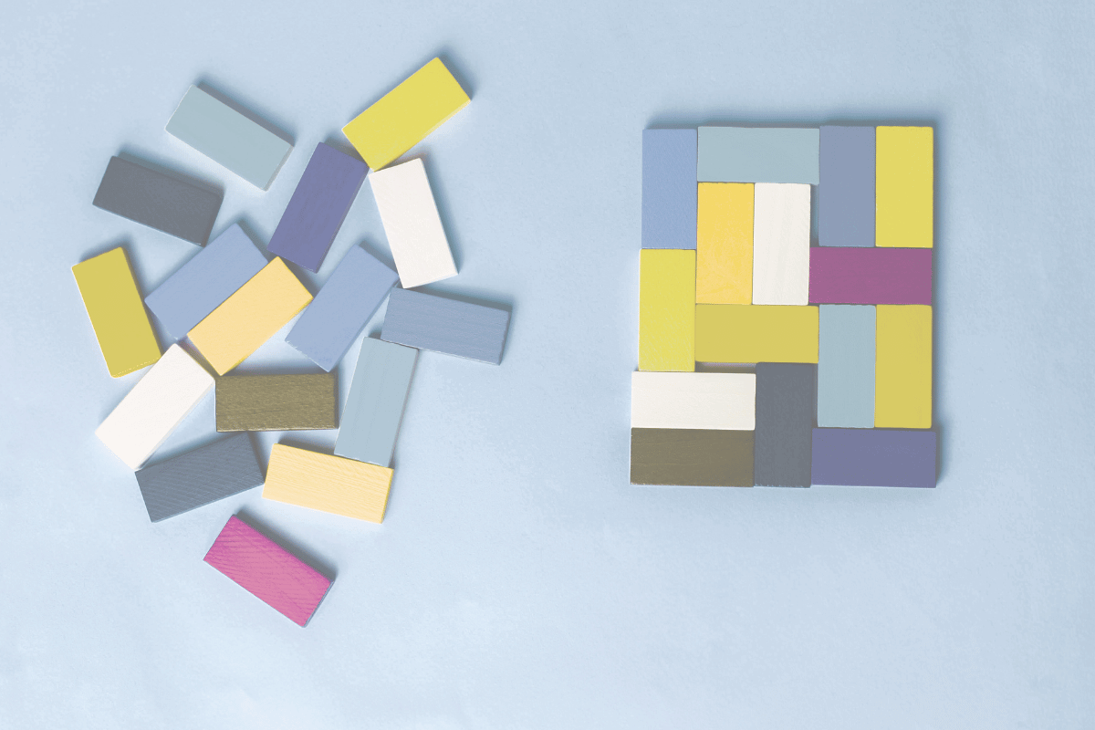 Bunte Holzklötze, einige lose, andere zu einer rechteckigen Struktur arrangiert, auf einem hellblauen Hintergrund.