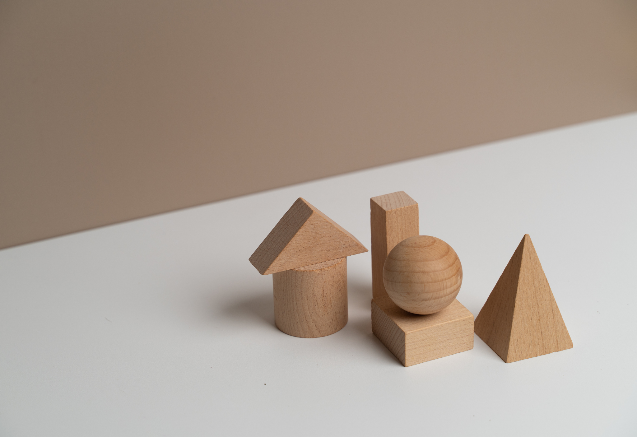 Verschiedene Holzformen auf weißem Hintergrund, inklusive Zylinder, Würfel, Kugel, Pyramide und Dreieck.