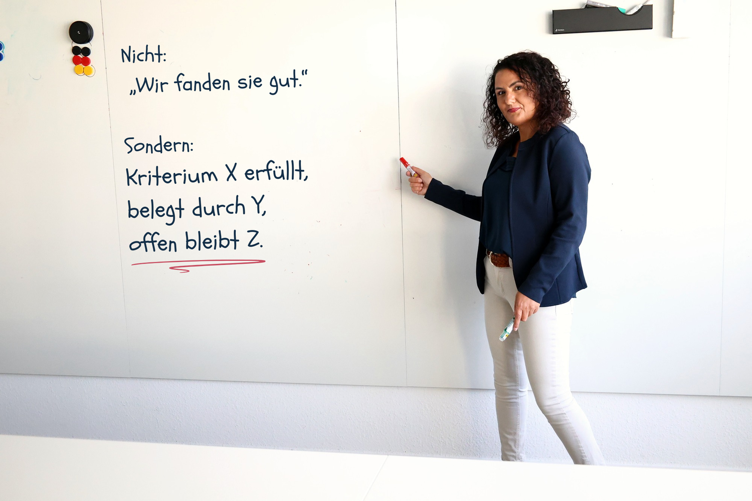 Audina Kamboua an einem Whiteboard. Darauf steht: Nicht „Wir fanden sie gut.“ Sondern: Kriterium X erfüllt, belegt durch Y.