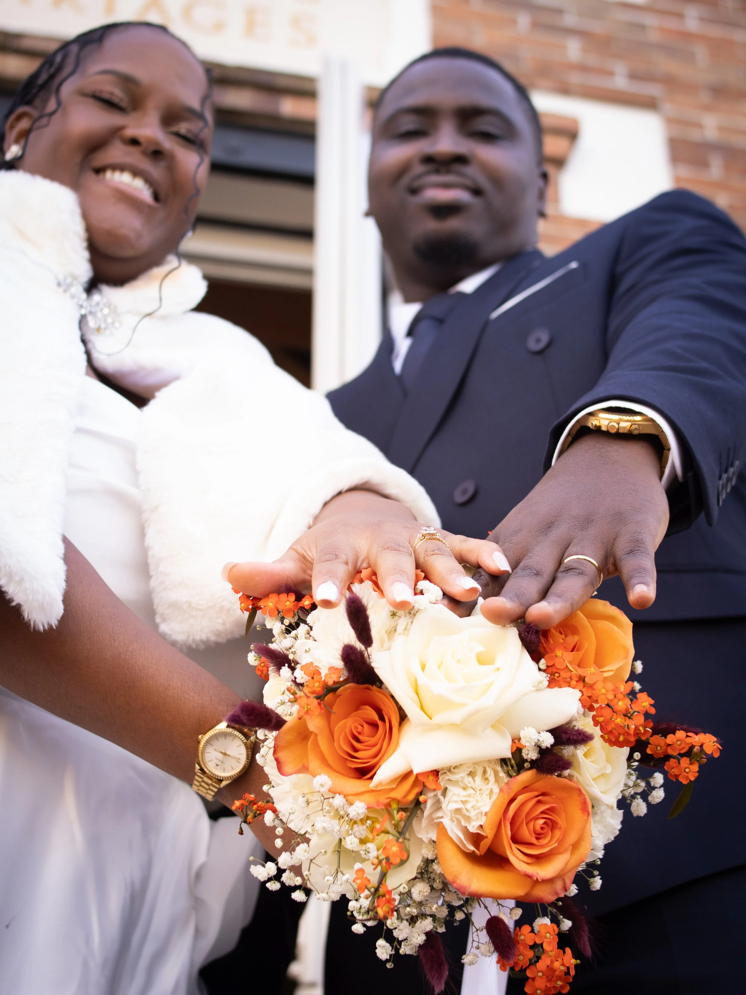 photographe de mariage pas chère en Essonne Un couple marié montrant leur alliance, tenant un bouquet de fleurs dans l'air, lors d'une cérémonie de mariage.