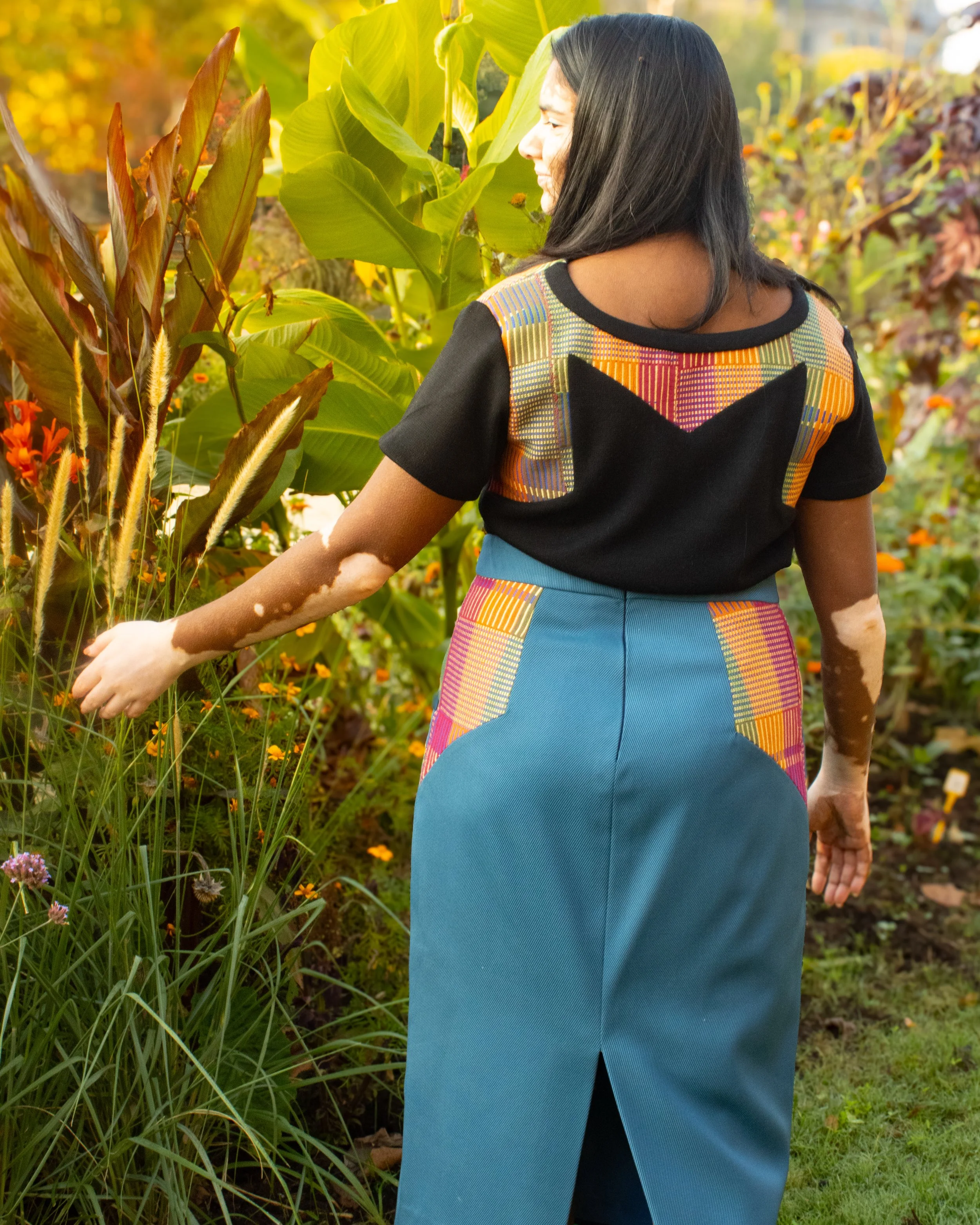 photographe b2b marque et e-Commerce Une femme vêtue d'une robe colorée, se tenant dans un jardin de fleurs, vue de dos.
