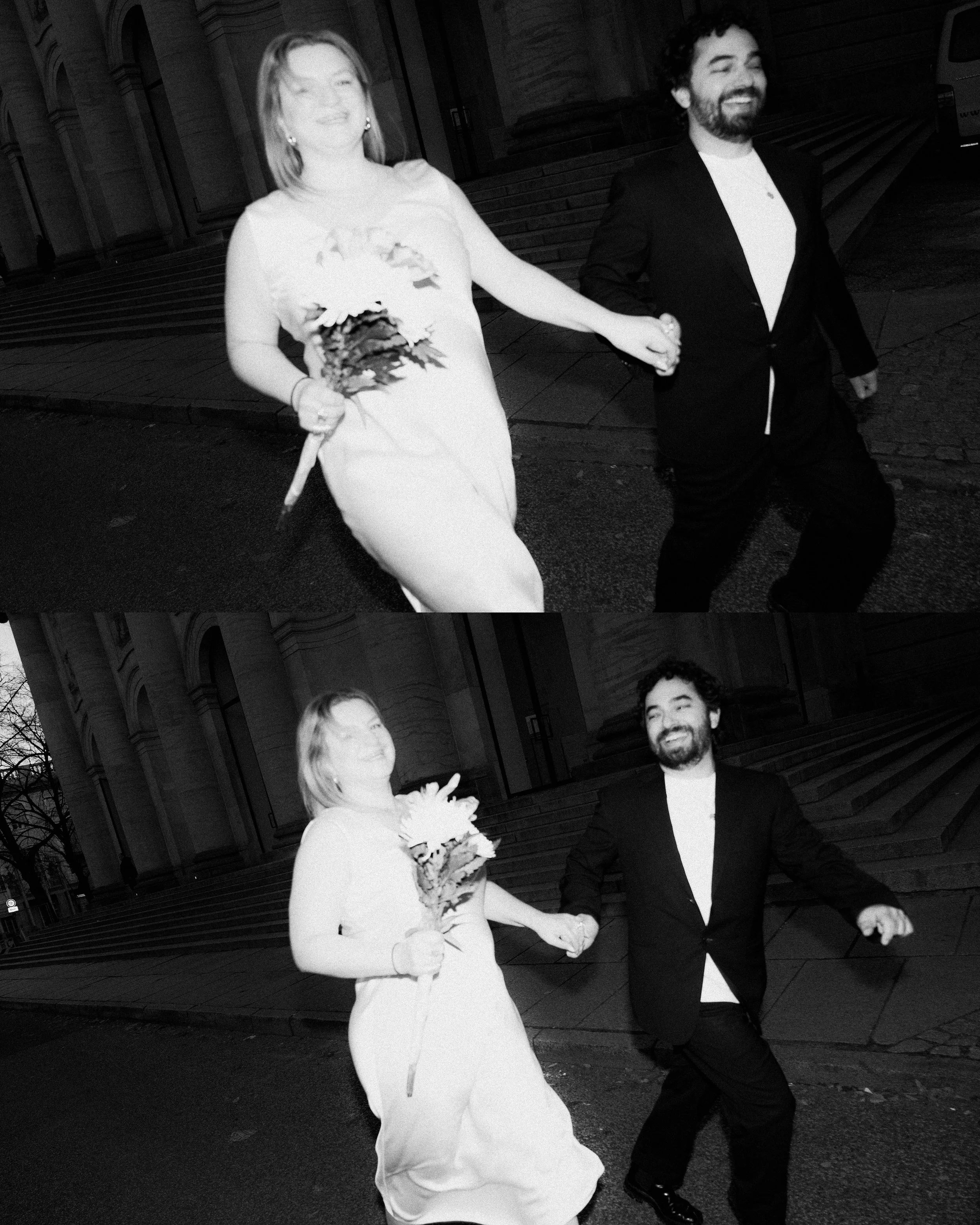 A black and white photo of a smiling woman in a white dress holding a bouquet and a man in a black suit holding hands and walking together outdoors in front of a building with steps.