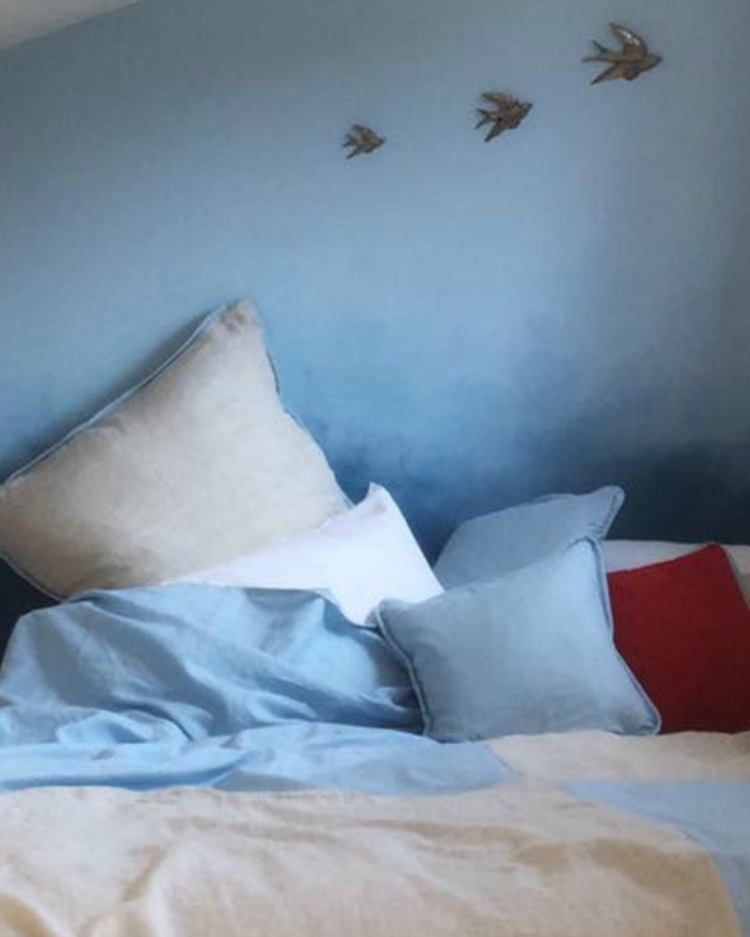 A bed with multiple pillows and a blue blanket, with decorative bird stickers on a blue wall above the bed.