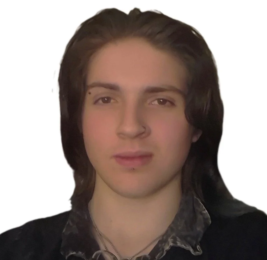 Portrait of a young person with long dark hair, fair skin, and facial piercings, looking at the camera against a plain background.