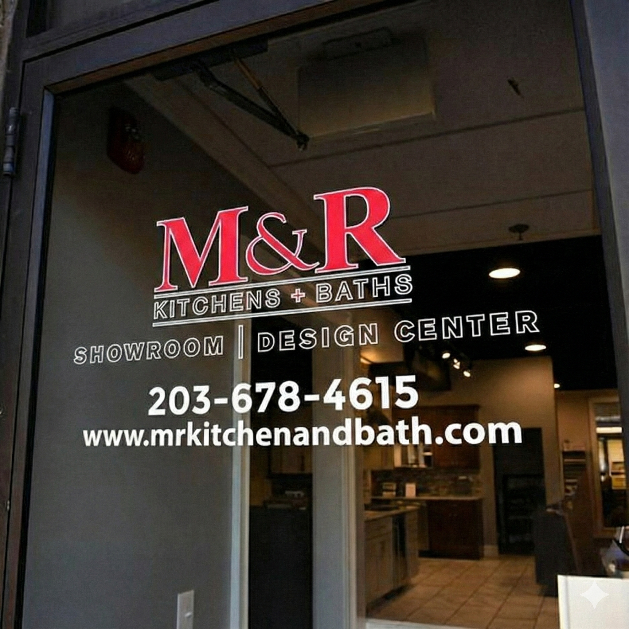 Glass front door to the M&R Kitchens + Baths showroom, featuring white vinyl lettering with their red logo, "SHOWROOM | DESIGN CENTER"