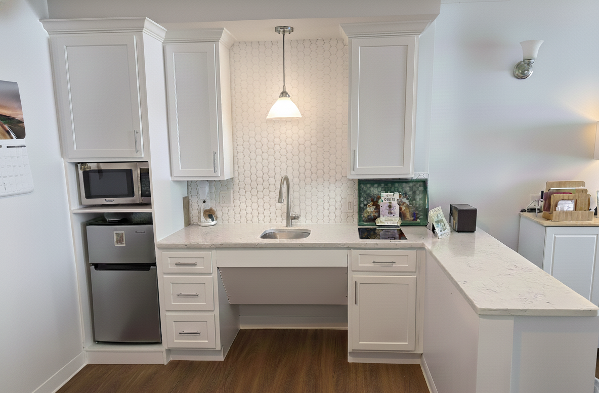 Clean, modern white kitchen featuring crown molding, a stainless steel refrigerator, white honeycomb backsplash, and an open, wheelchair-accessible sink area, located in Shelton, CT.