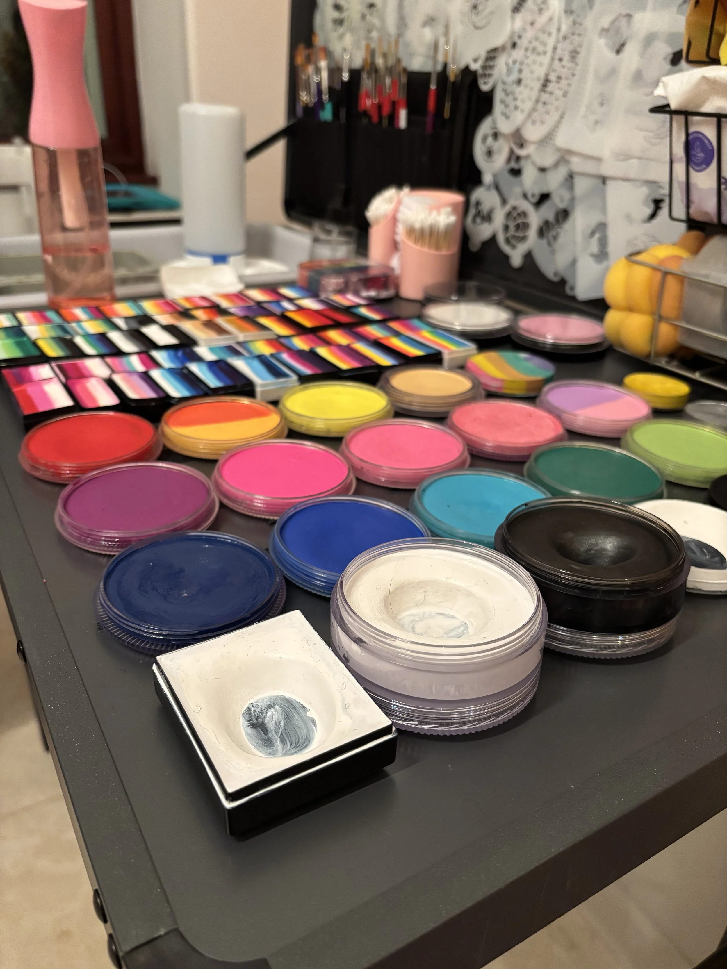 A makeup artist's workstation with various brightly colored eyeshadows, face powders, and makeup brushes arranged on a black table.