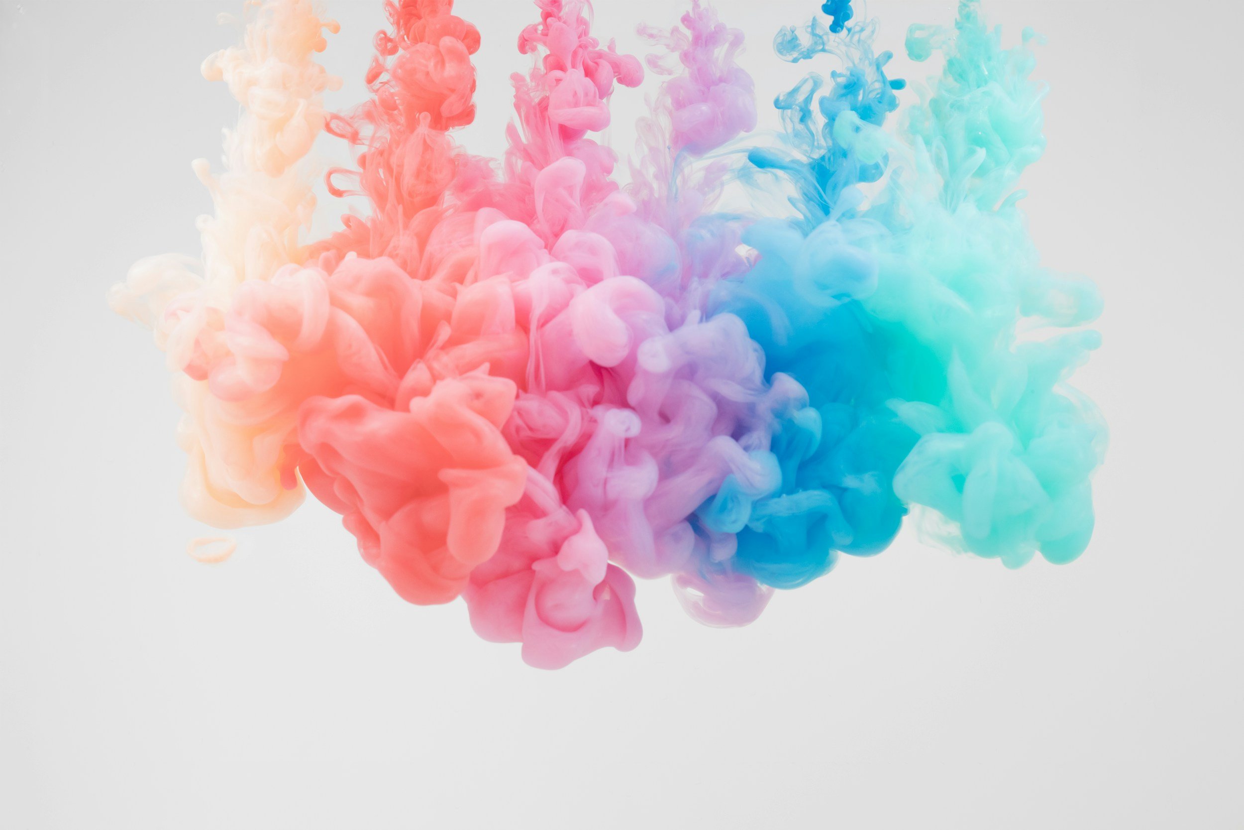 Colored ink dispersing in water creating clouds of pink, purple, blue, and teal on a light background.