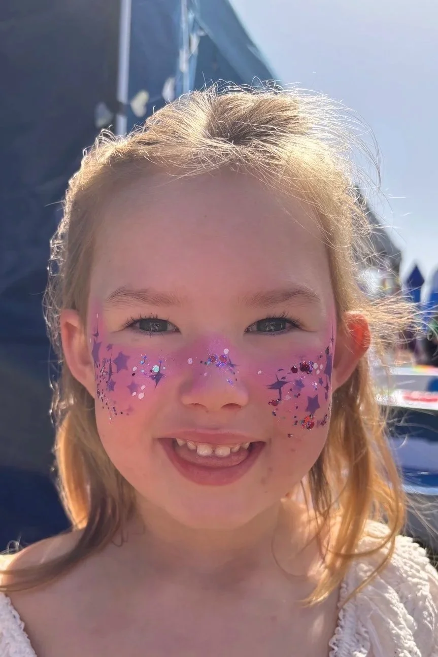 Young girl wearing pink and purple festival glitter face paint with stars and sparkles