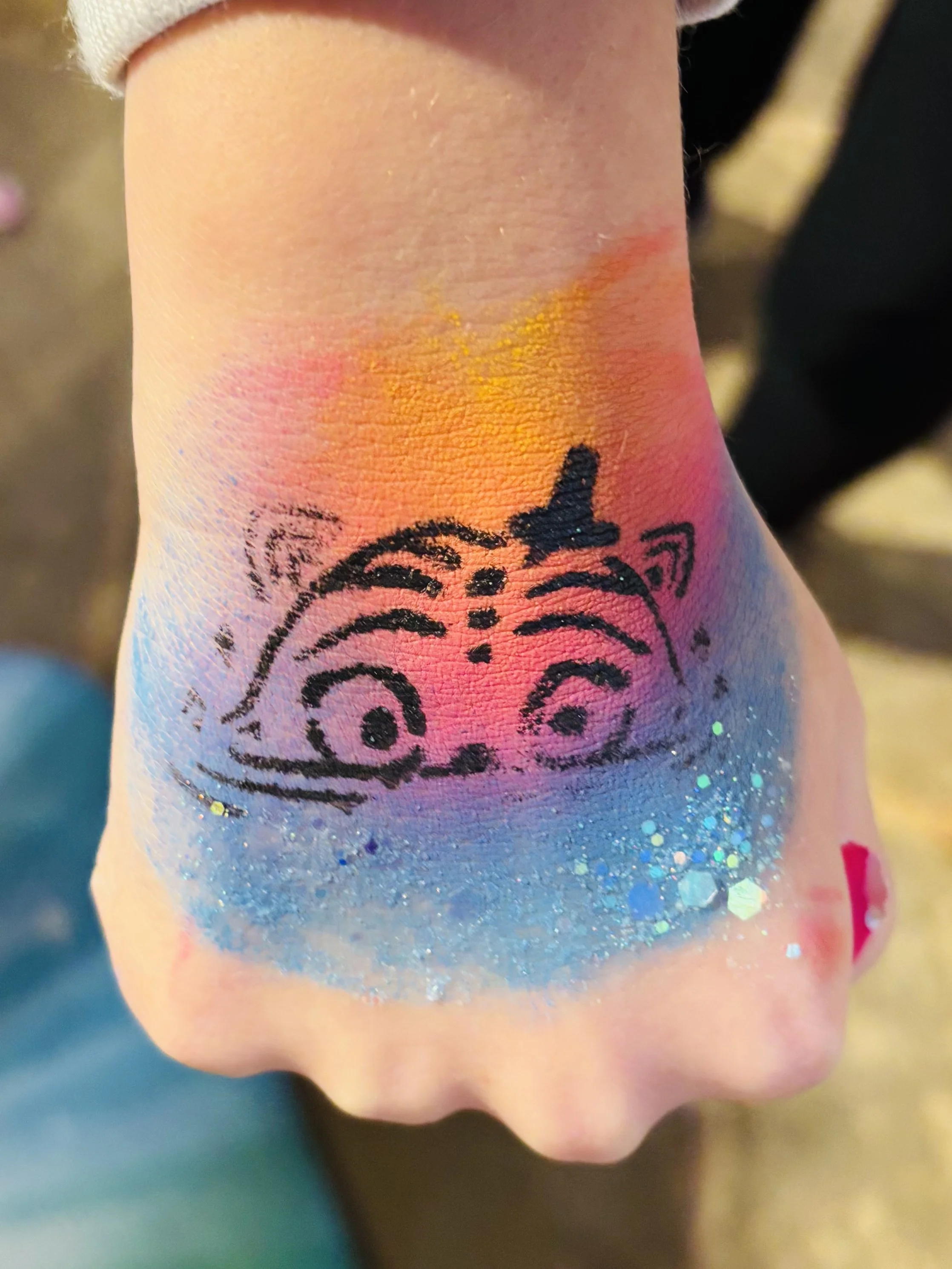 Temporary tattoo of a tiger's face on a person's hand with colorful glitter and rainbow-colored background.