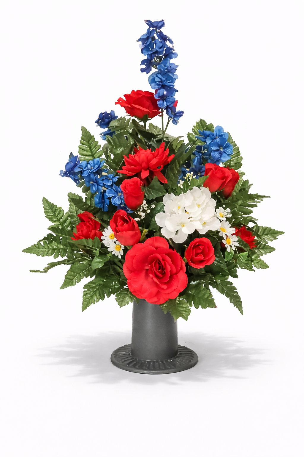 Flower arrangement in a gray vase, featuring red roses, red dahlias, white orchids, blue delphiniums, small white daisies, and green fern leaves.
