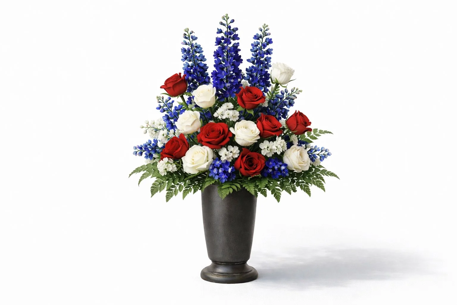 A floral arrangement with red, white, and blue flowers in a black vase, featuring roses, delphiniums, and ferns.