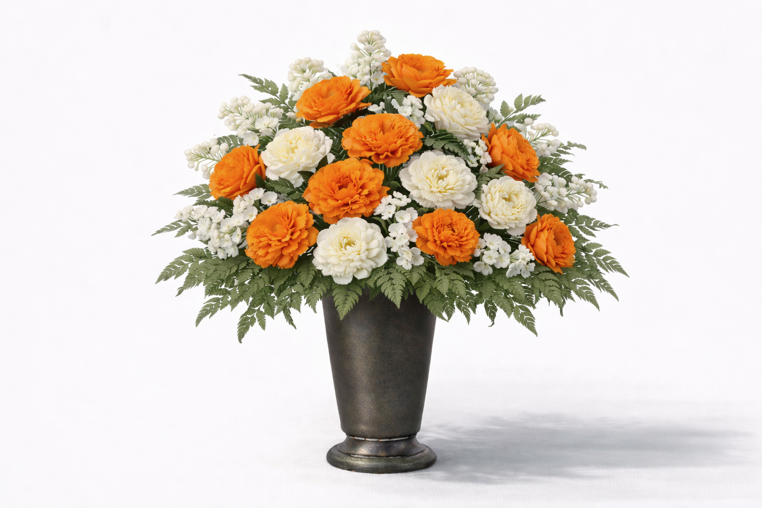 A floral arrangement with orange and white flowers in a metallic gray vase, surrounded by green fern leaves.