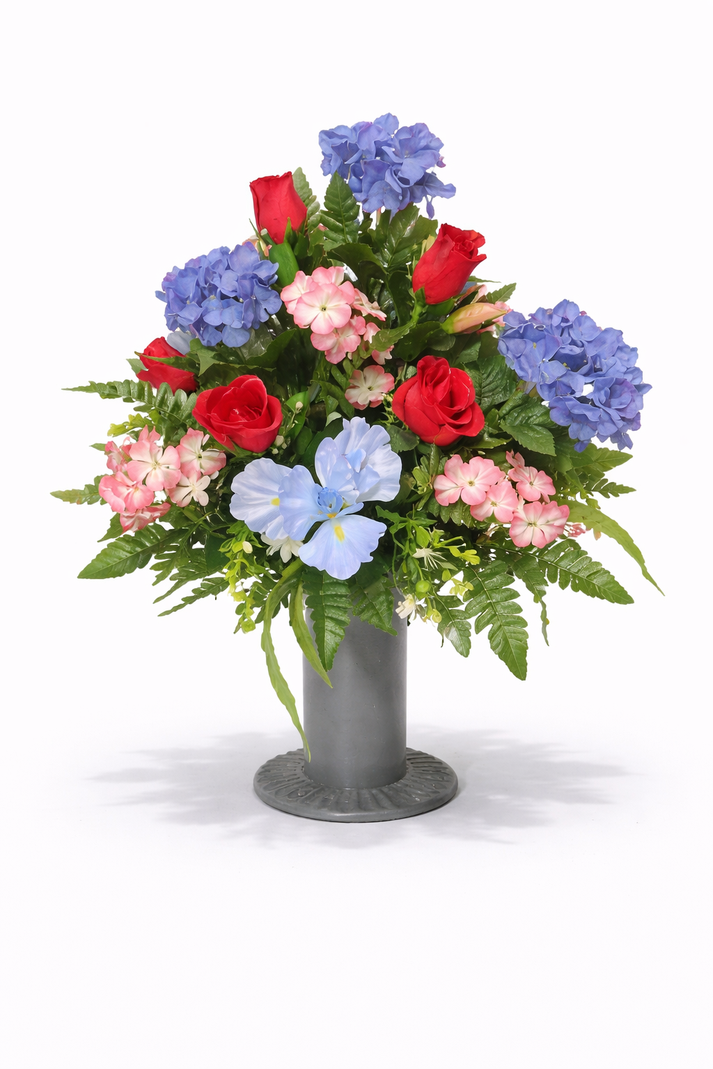 A floral arrangement with red roses, blue hydrangeas, pink and white impatiens, and green foliage in a gray vase.