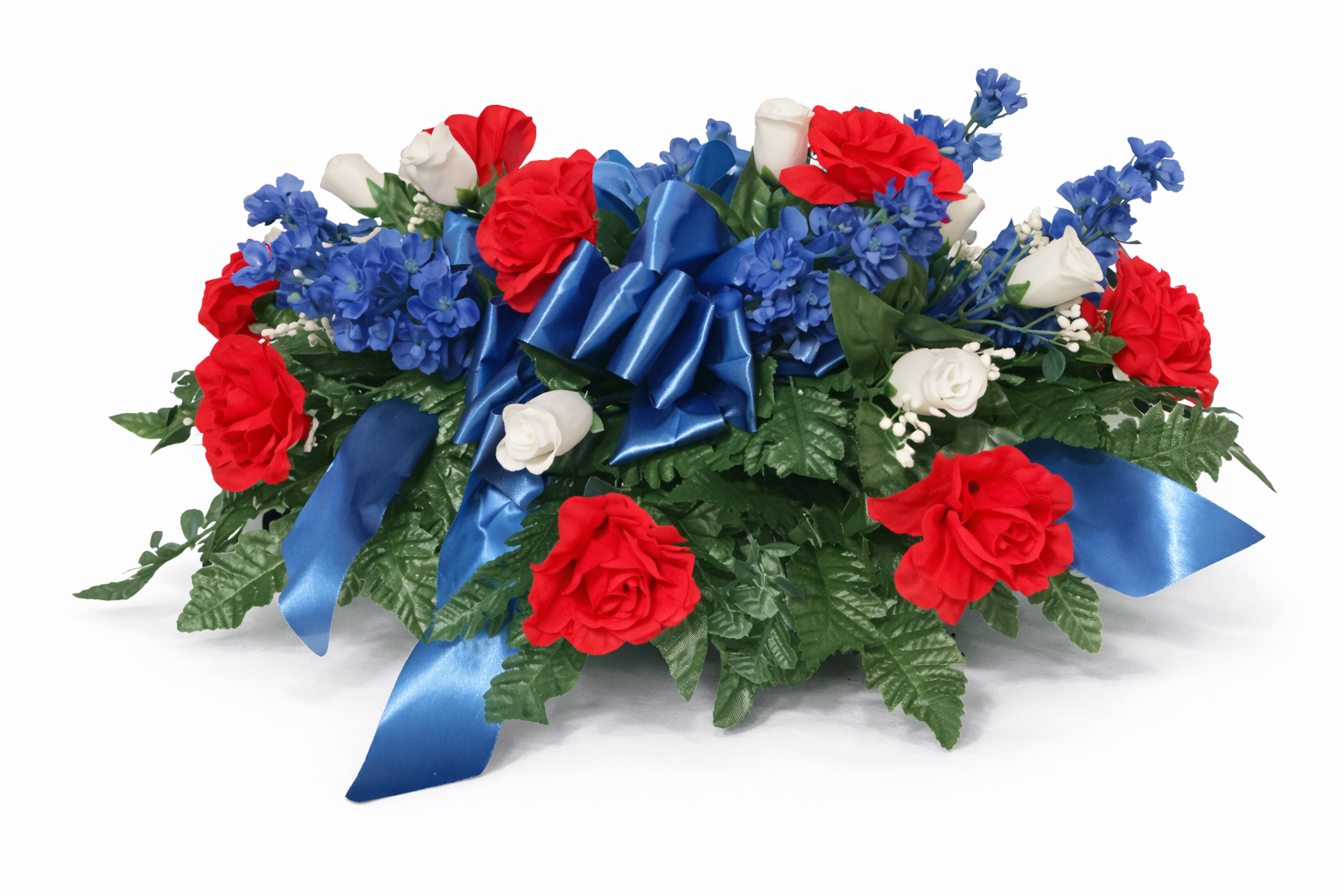 Flower arrangement with red, white, and blue flowers, large blue satin ribbons, and green leaves.