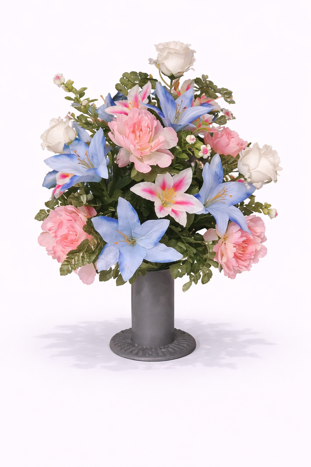 A floral arrangement of pink roses, blue lilies, and white roses in a gray vase on a white background.