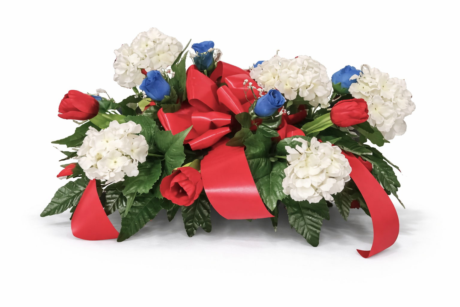 A floral arrangement with white hydrangeas, red tulips, and blue roses, accented with greenery and a red ribbon.