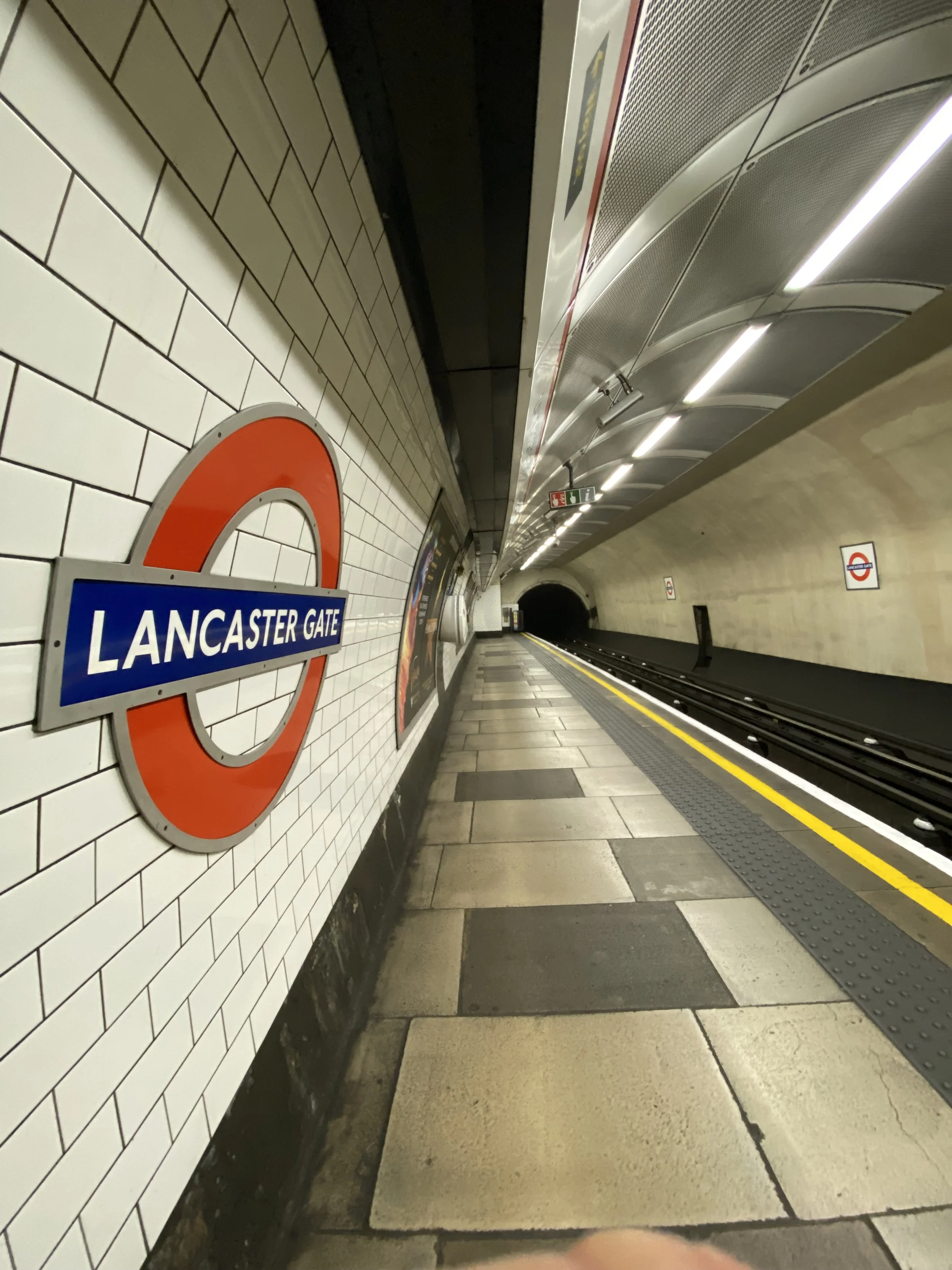 Togstasjon under jord med plattform, skilt for Lancaster Gate, og London Underground-symbolet på veggen. Plattformer er tomme, og tunnelen strekker seg inn i mørket.