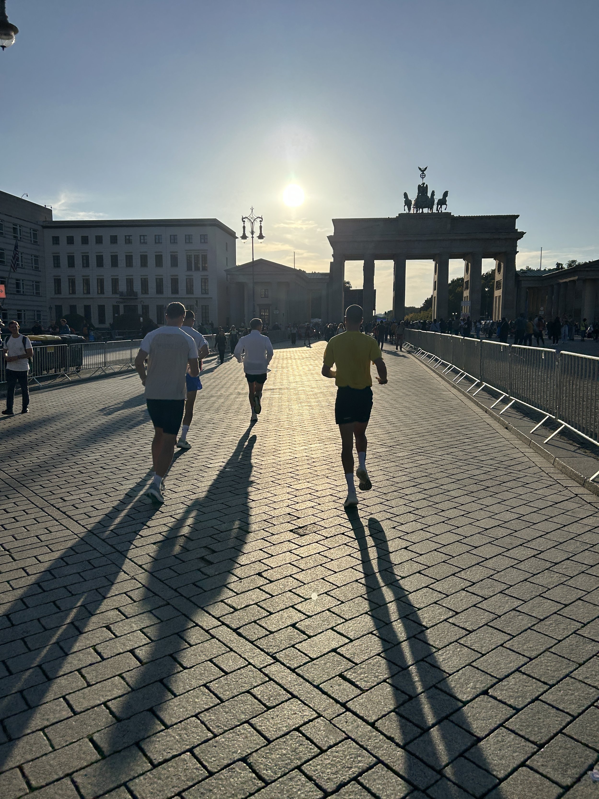 Mennesker som løper foran Brandenburger Tor i Berlin med solen lavt på himmelen.