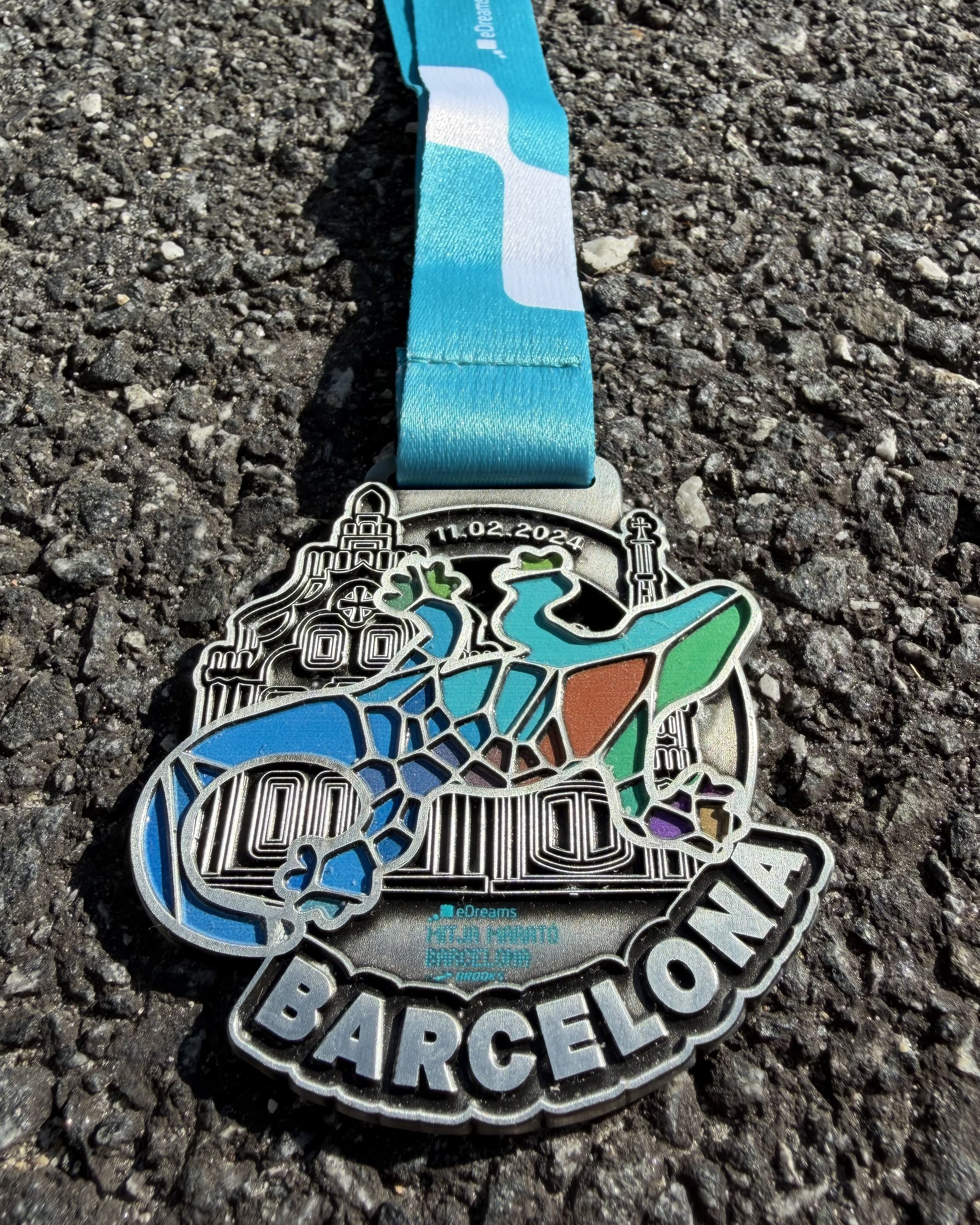 En medalje med et utformet utseende av due, som er pyntet med farger som blå, grønn, oransje, lilla og svart, plassert på en grusunderlag.