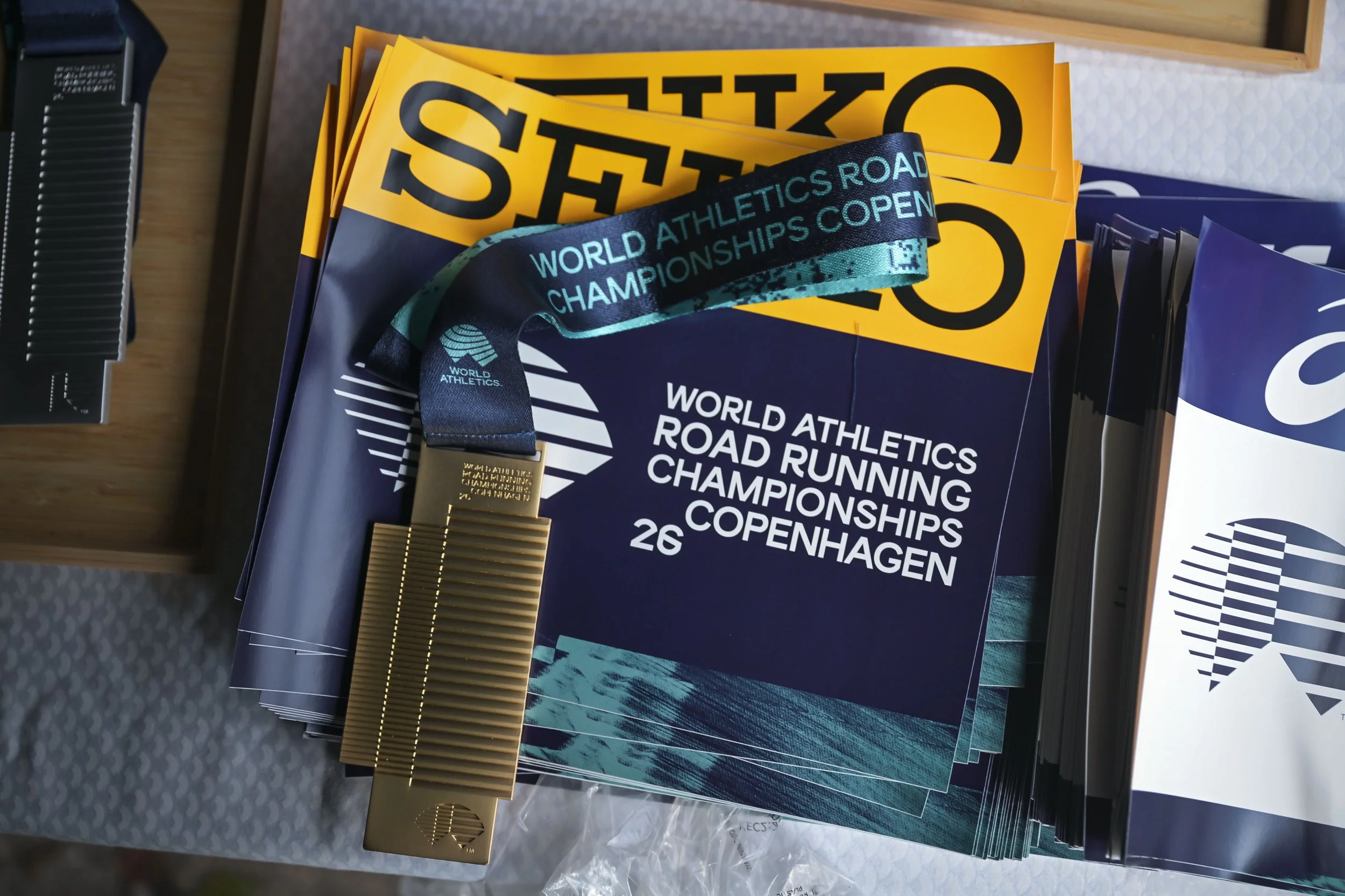 Toppkvalitet medalje med World Athletics Road Running Championships København 2022 skrevet på den, omgitt av plakater for mesterskapet.