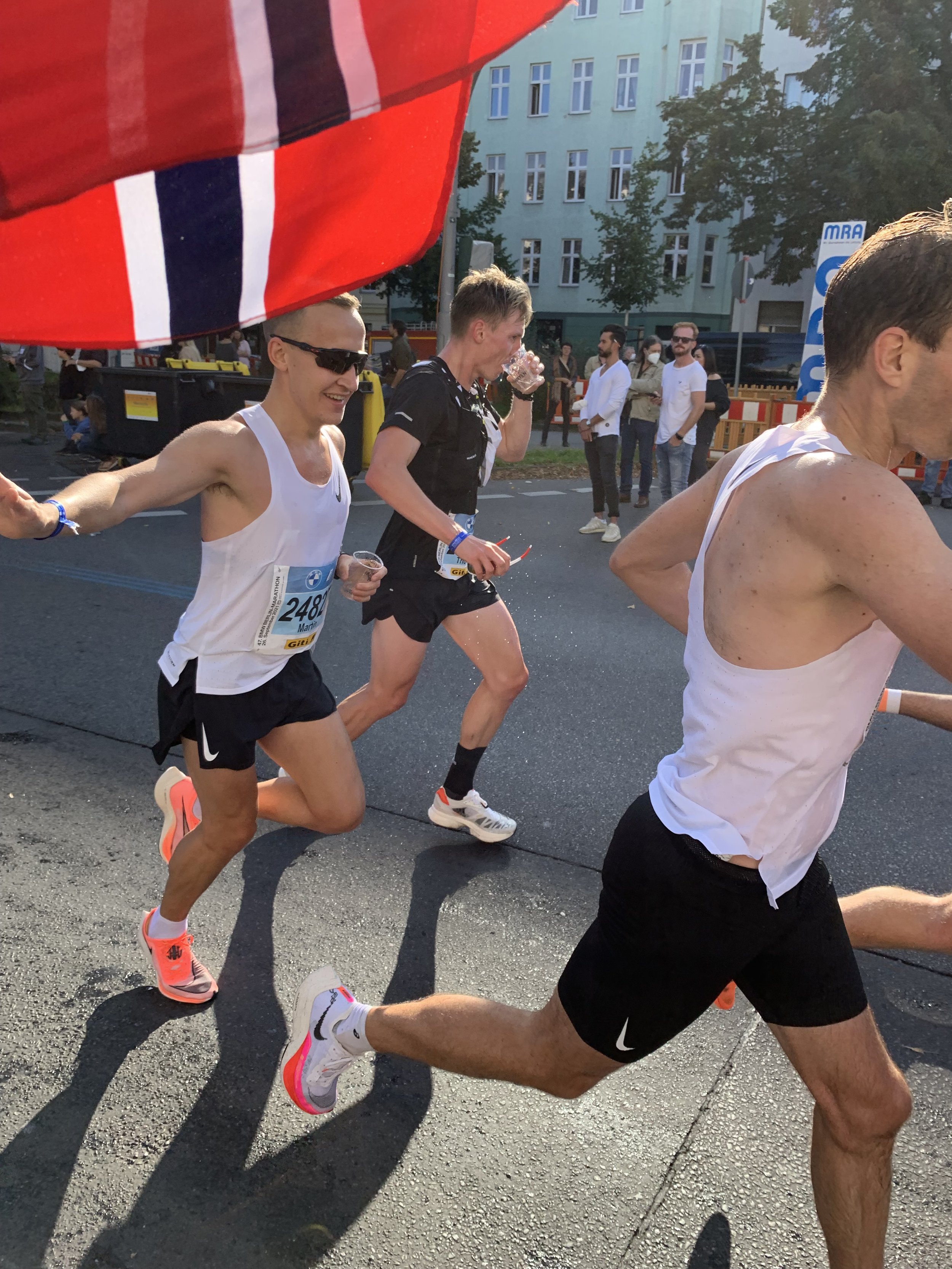 Bilde av løpere midt i et maratonløp i en by, med bygninger og folk som ser på i bakgrunnen.