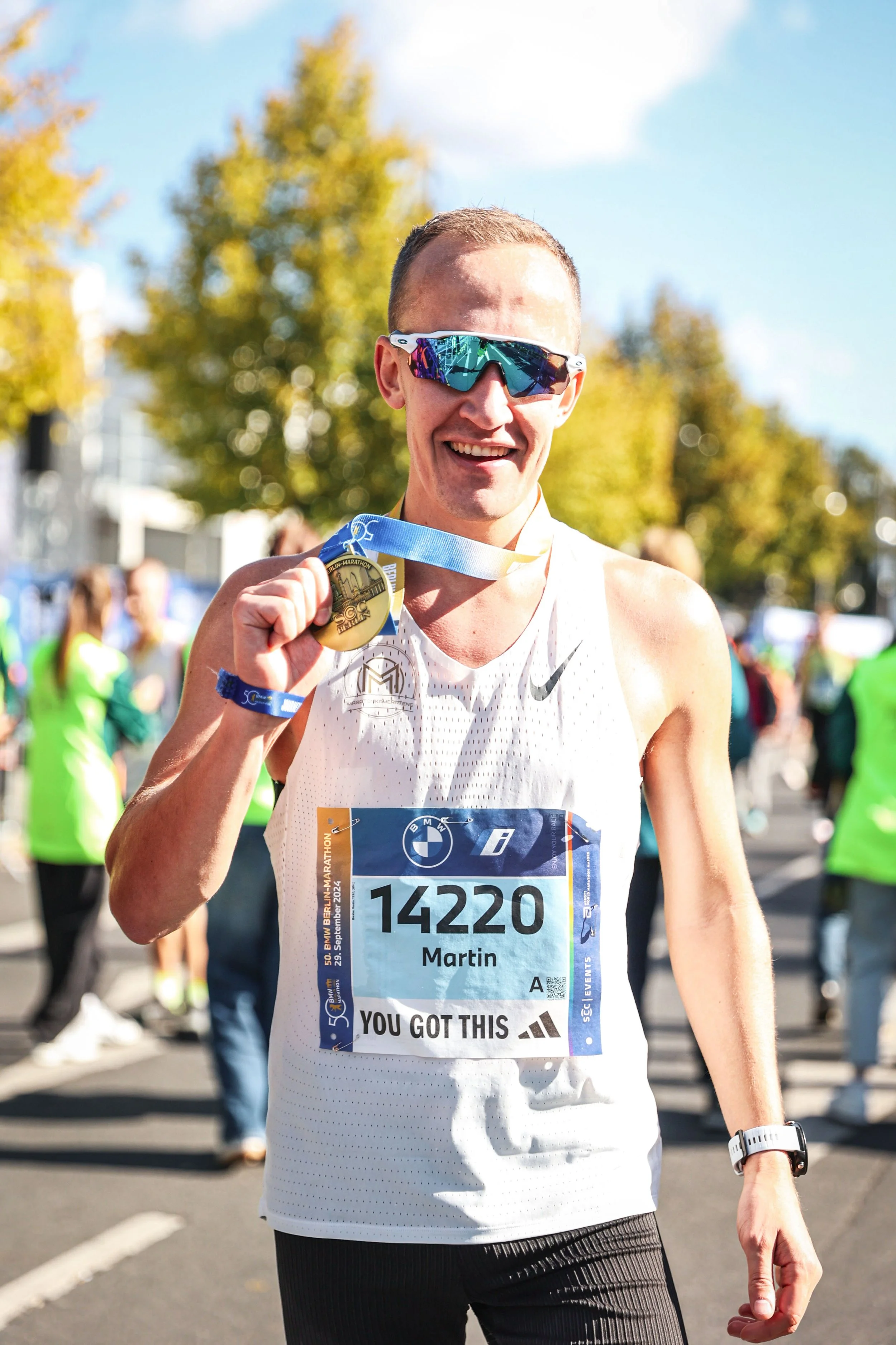 En mann som har fullført et maraton, smiler og holder opp en medalje rundt halsen sin