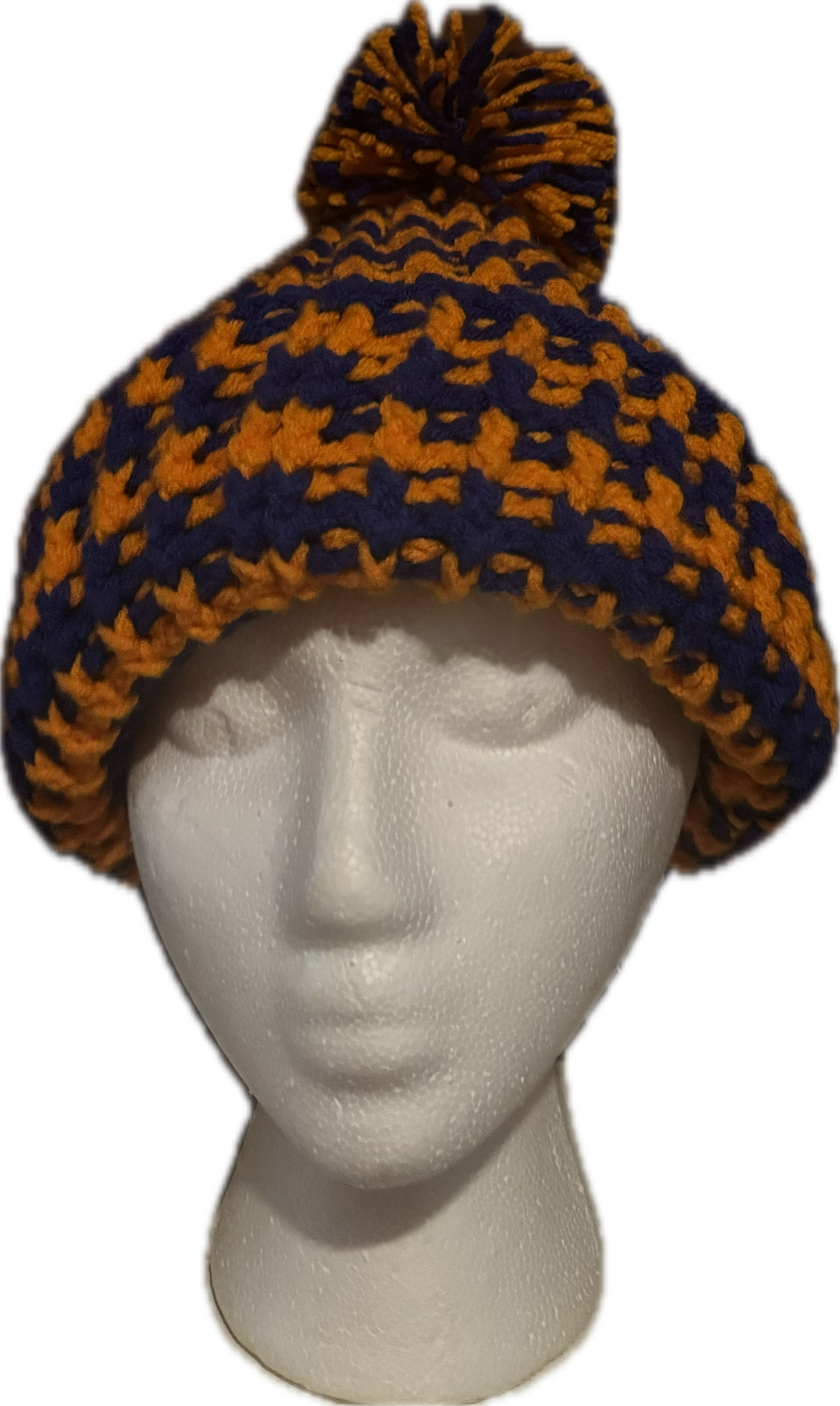 A crochet hat with a multicolored pattern of orange and dark blue, featuring a pom-pom on top.